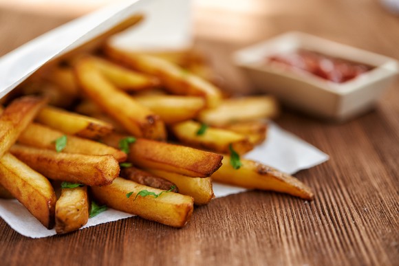 Close-up shot of some golden brown french fries, sprinkled with dill. In the background, you see an out-of-focus ketchup container.