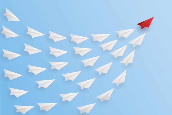 A swarm of white paper airplanes led by a single red paper airplane.