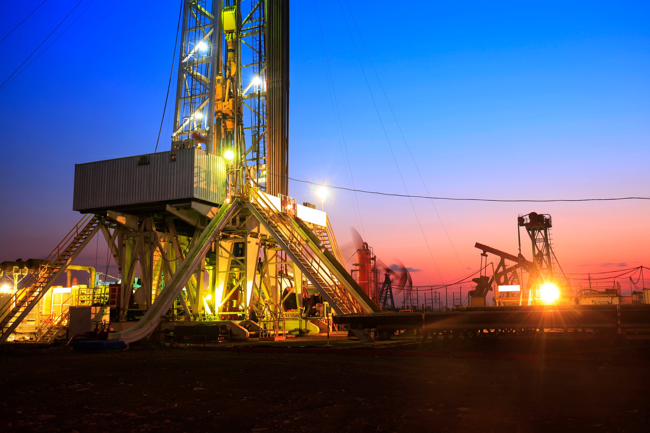 Drilling rigs lit up at dusk.