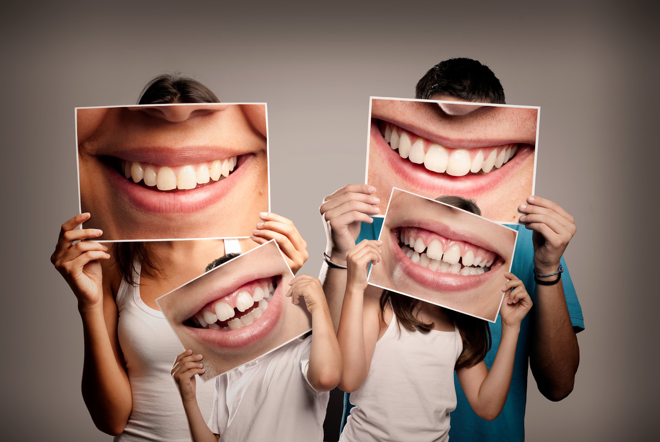 Man, woman, and two children holding pictures of smiles showing teeth in front of their faces