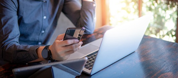 A man sitting in front of a laptop and using a mobile phone