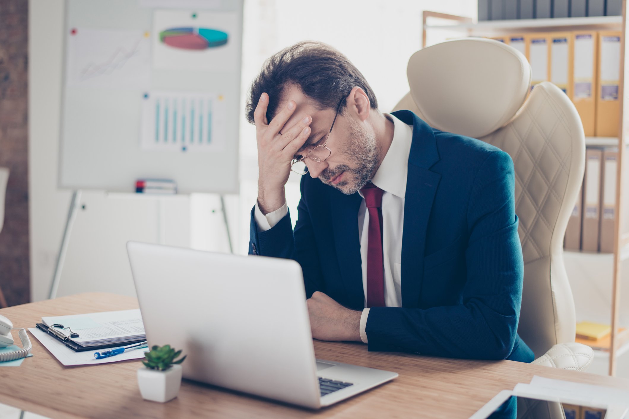 Man in suit at laptop holding head