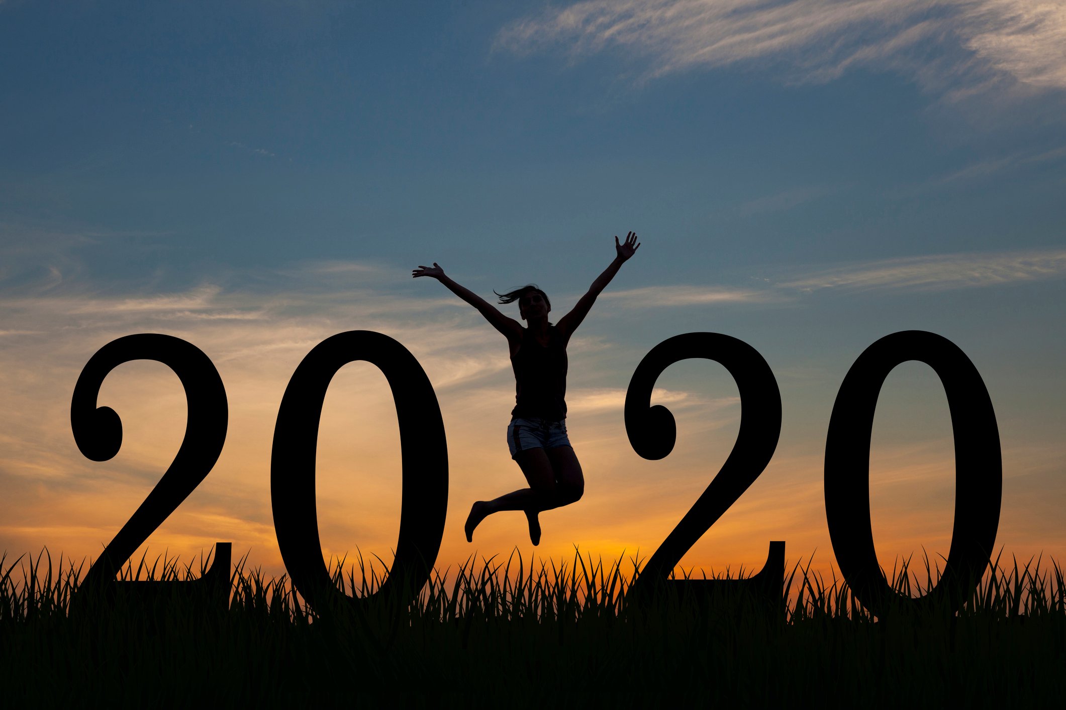 A large sign that reads 2020 against a sunset with a woman jumping off the ground in between the two twenties. 