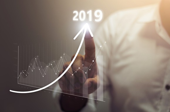 A businessman touches a digital chart which shows an upward arrow pointing to 2019.