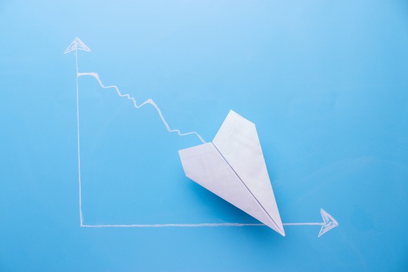 A declining chart with the arrow on the trendline represented by a paper airplane.