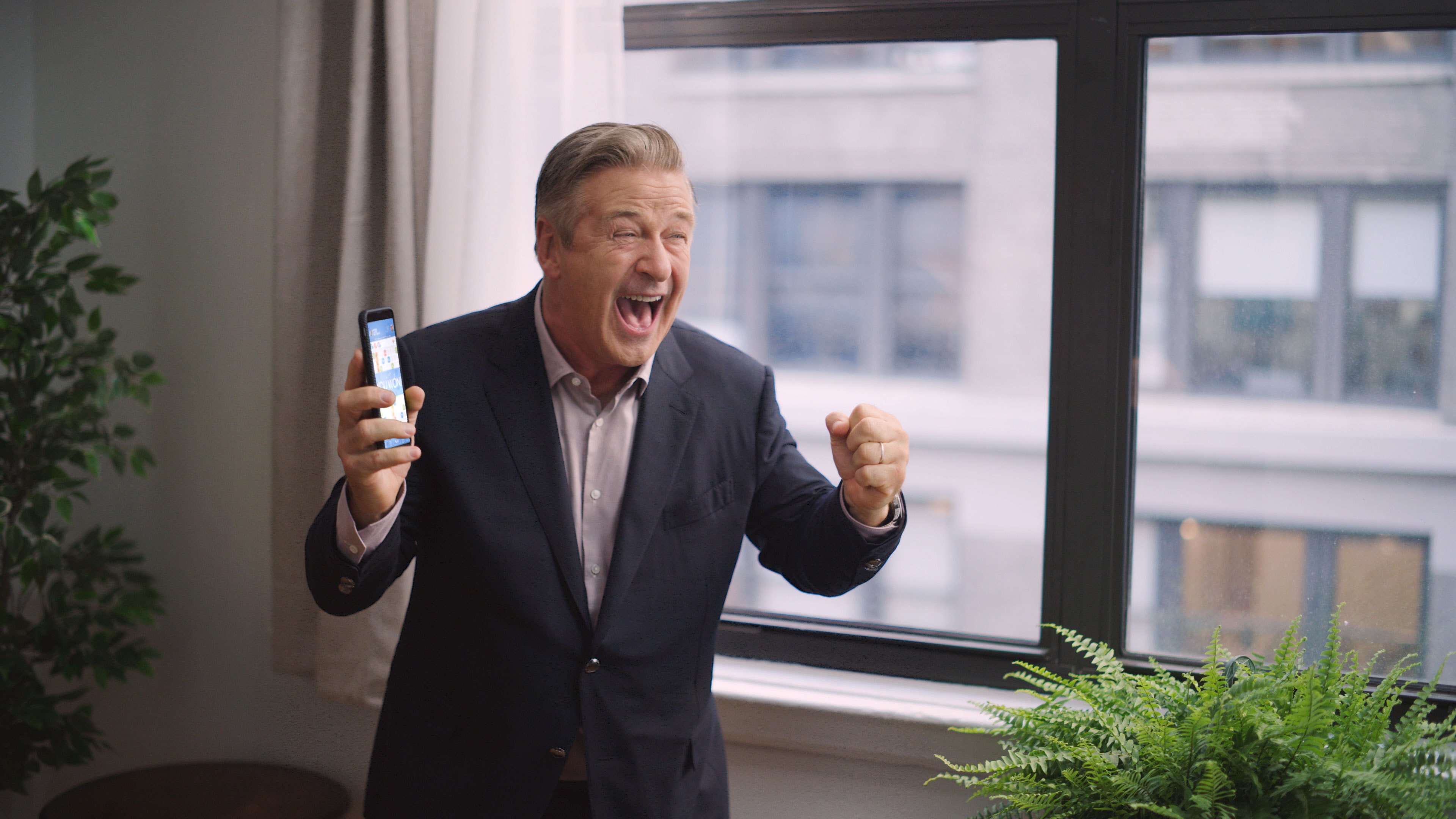 Actor Alec Baldwin celebrates while holding a smartphone in his hand that is running Zynga's Words with Friends game.