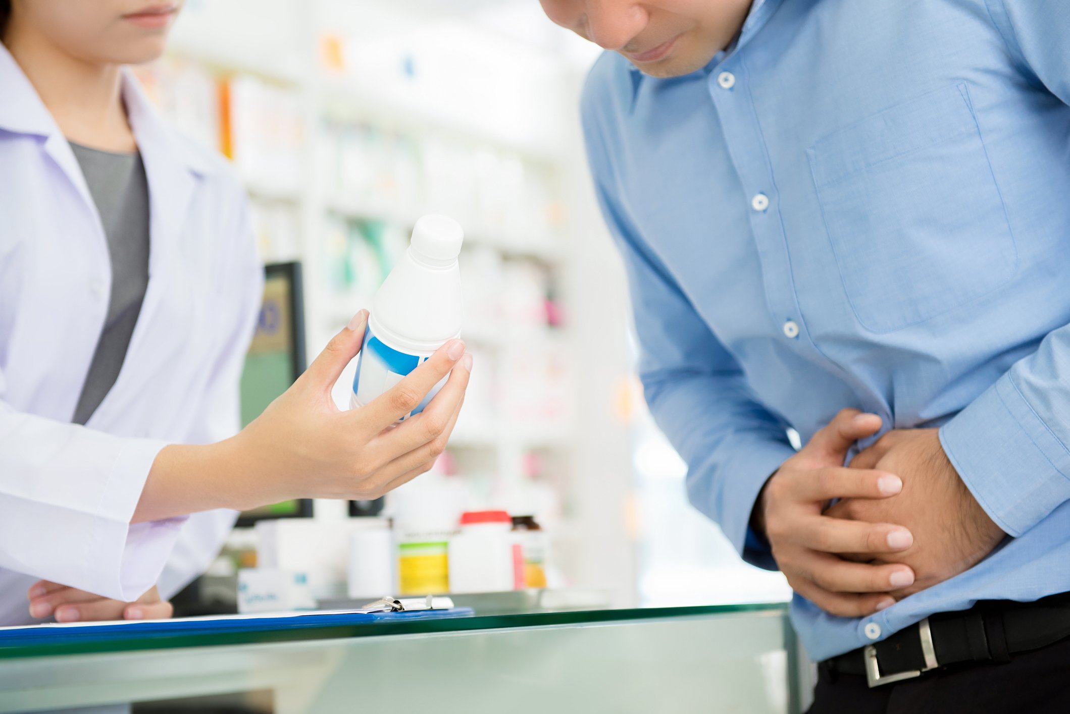 A man holding his stomach being given a prescription from a pharmacist.