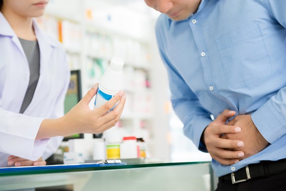 A man holding his stomach being given a prescription from a pharmacist.