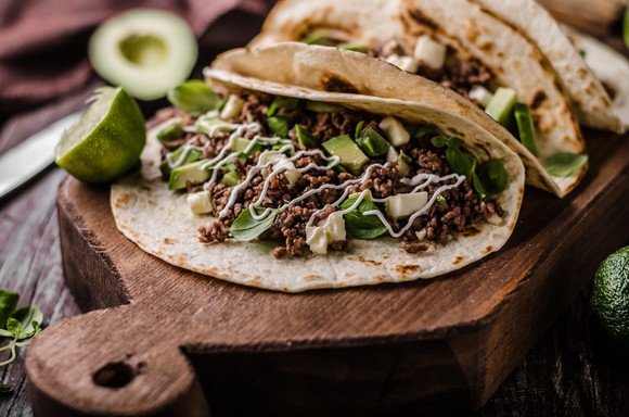 A taco on a wooden platform serving board.