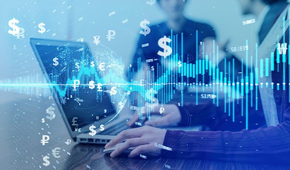 A person's hands on a laptop computer surrounded by dollar signs and symbols for other global currencies.