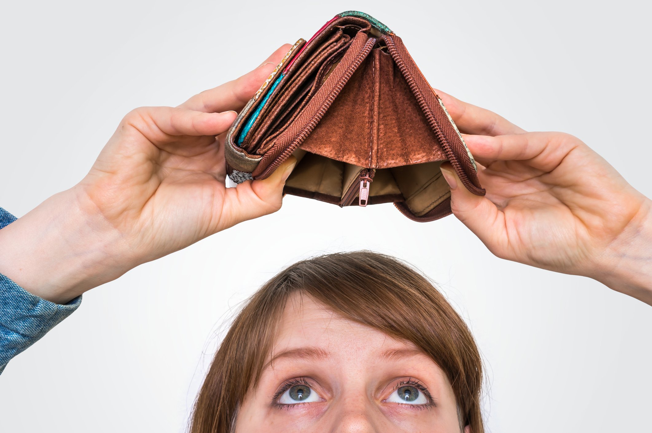 A woman looks up at an open and empty wallet she's holding over her head.