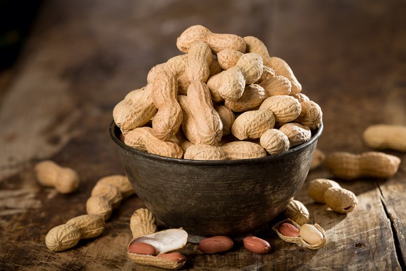 A bowl of peanuts sits on a wooden table.