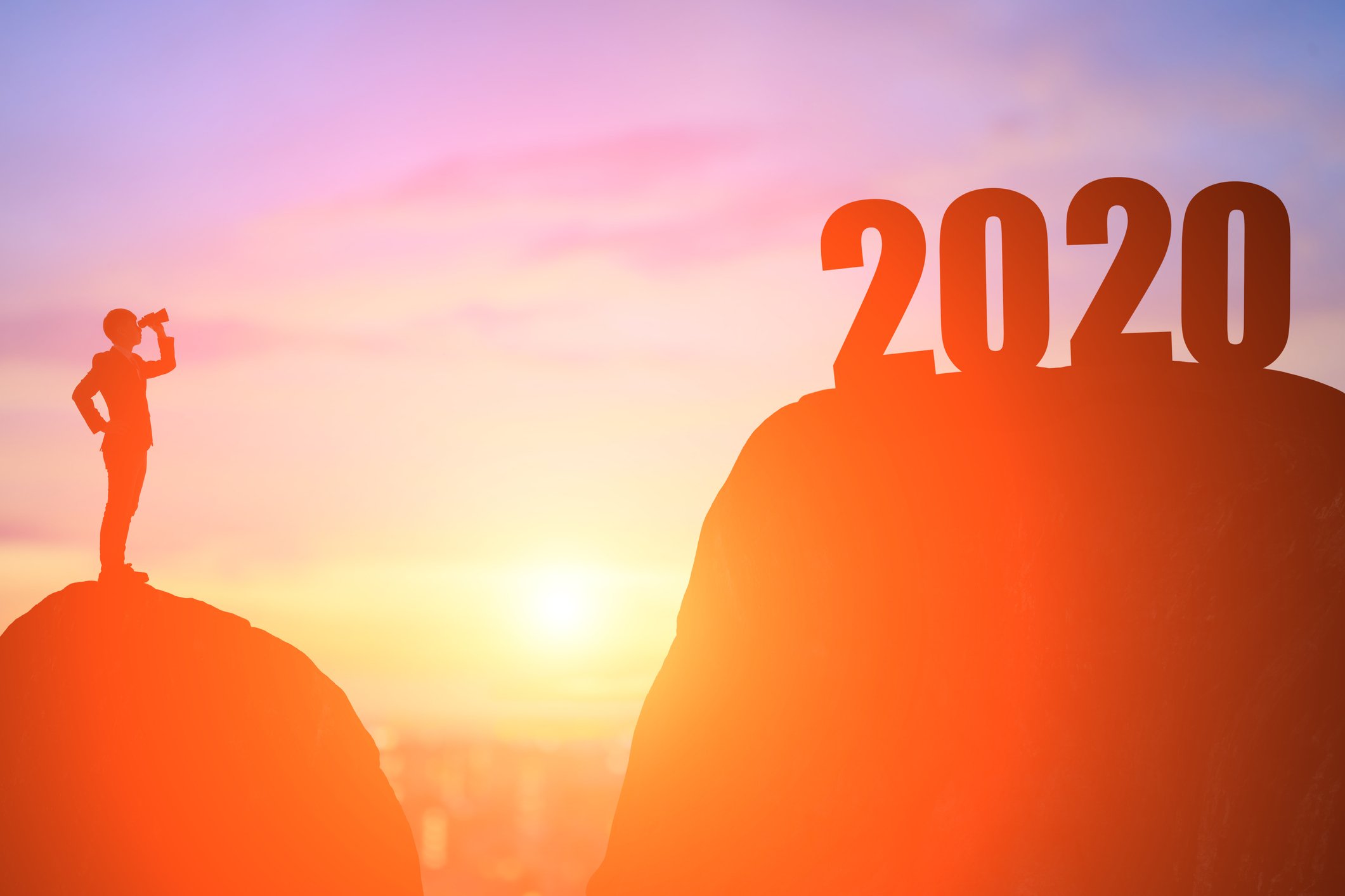 Silhouette of a man on a hill looking through binoculars at 2020 on top of a nearby hill