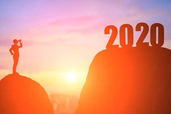 Silhouette of a man on a hill looking through binoculars at 2020 on top of a nearby hill