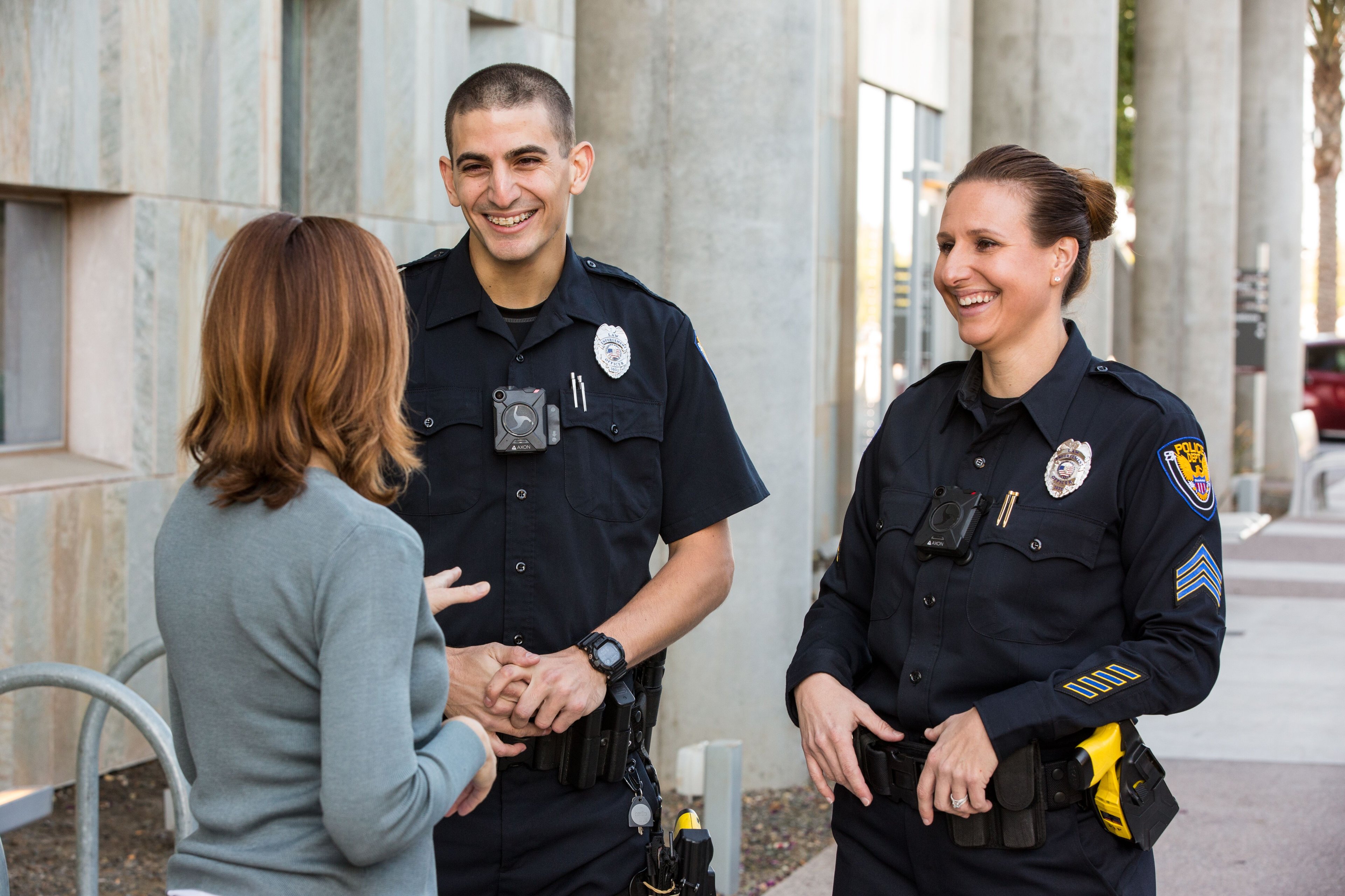 Two police officers wearing body cameras chat with a citizen.