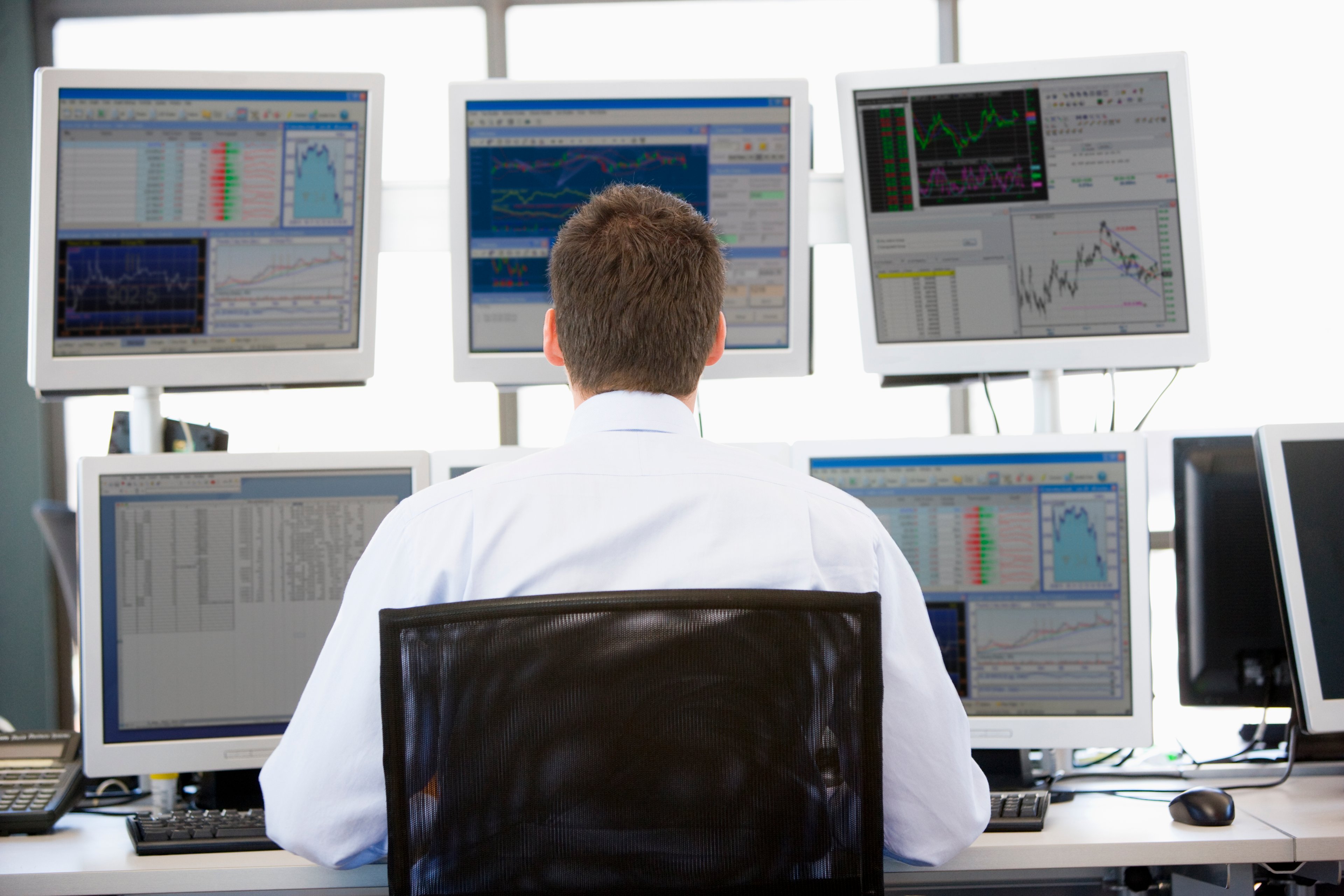 A man looks like at five computer screens showing stock movement