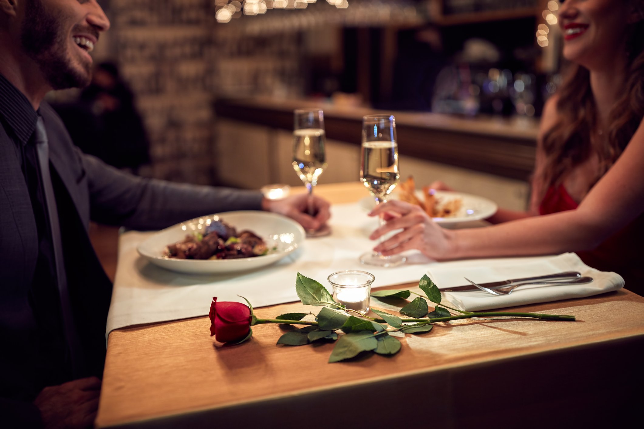 Man and woman eating dinner at restaurant table with wine glasses in their hands.