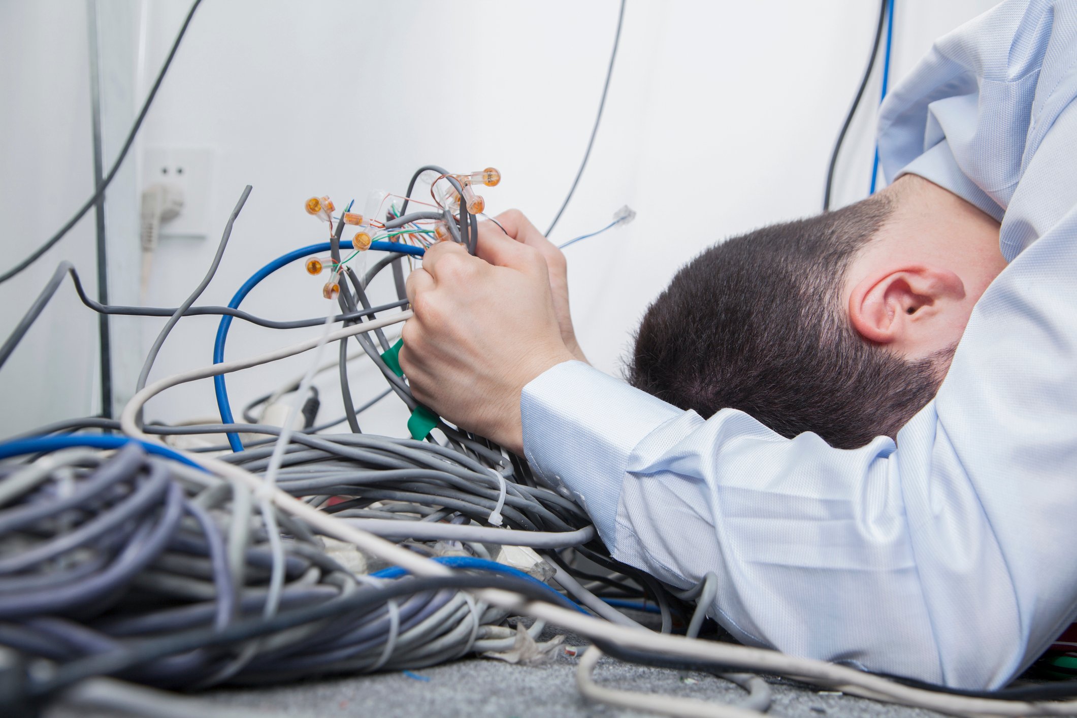Facing a messy pile of disorganized network cables, a technician hold the cables by the handful and leans forward to rest his forehead on the floor.