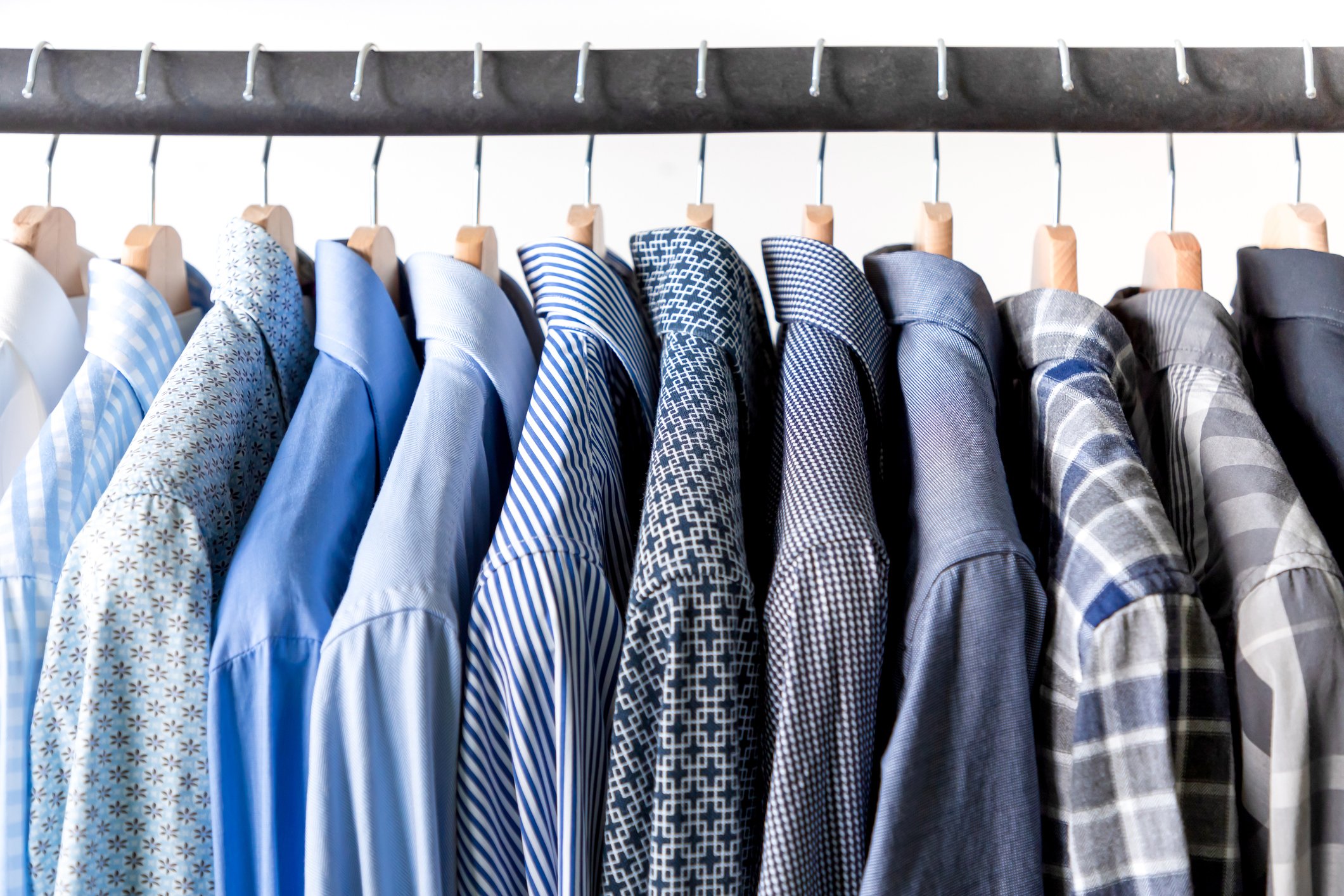Dress shirts in various shades of blue and gray hang on a rack.