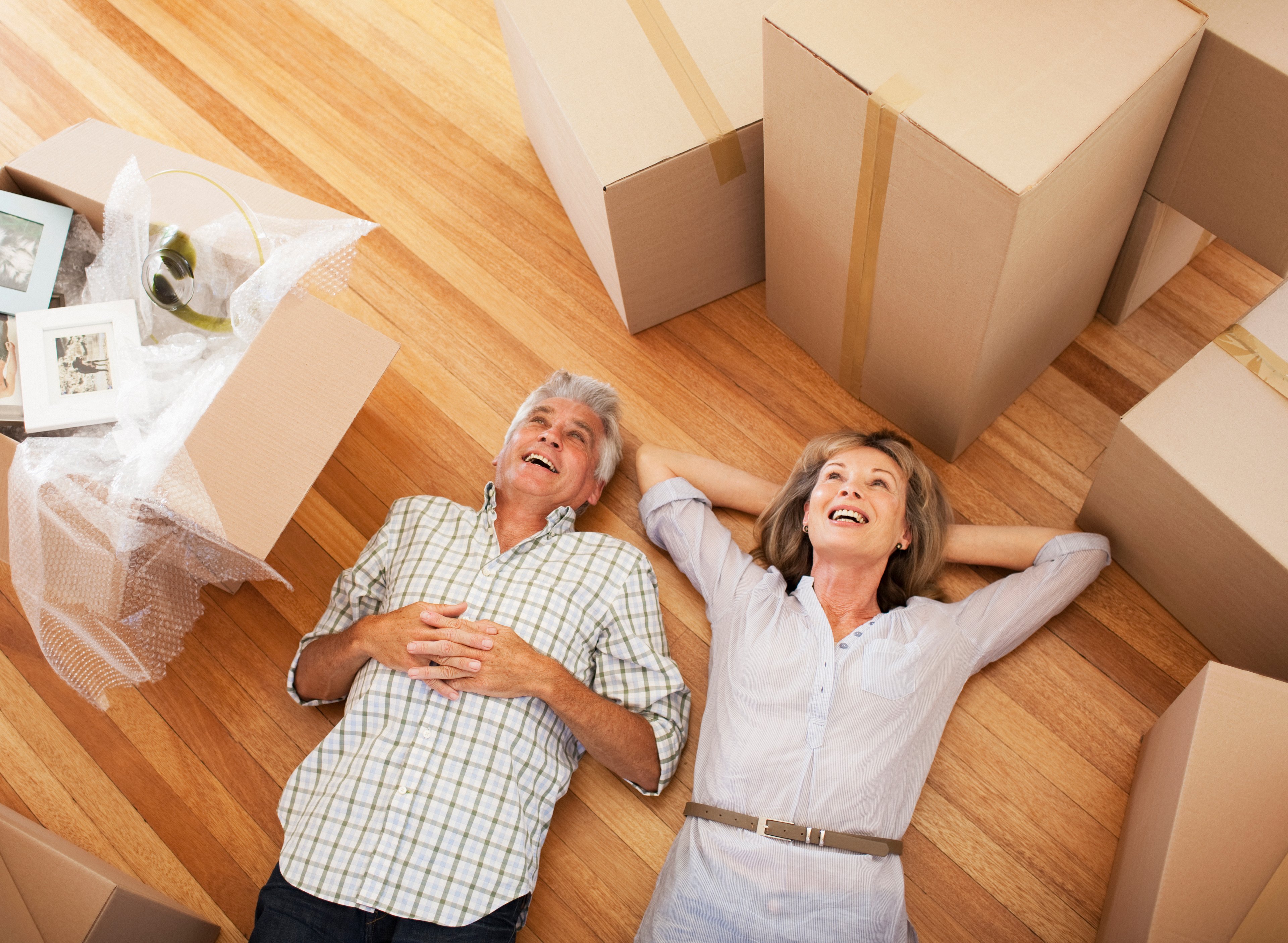 Older couple laying on floor in the middle of moving boxes.