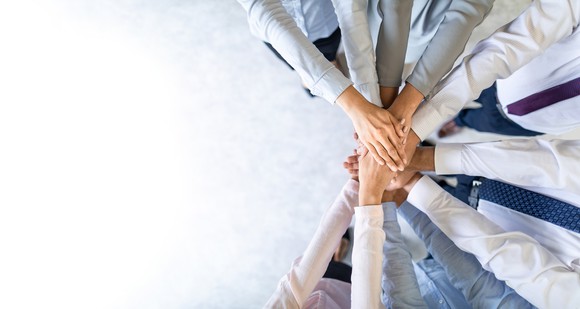 Photograph of business team putting their hands together, like a sports team starts a game.