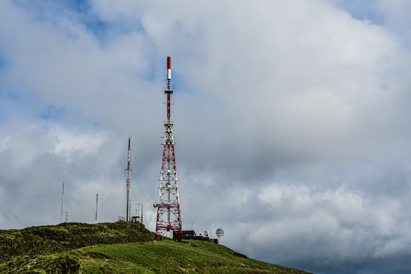 Several cell towers stand atop a green hill.