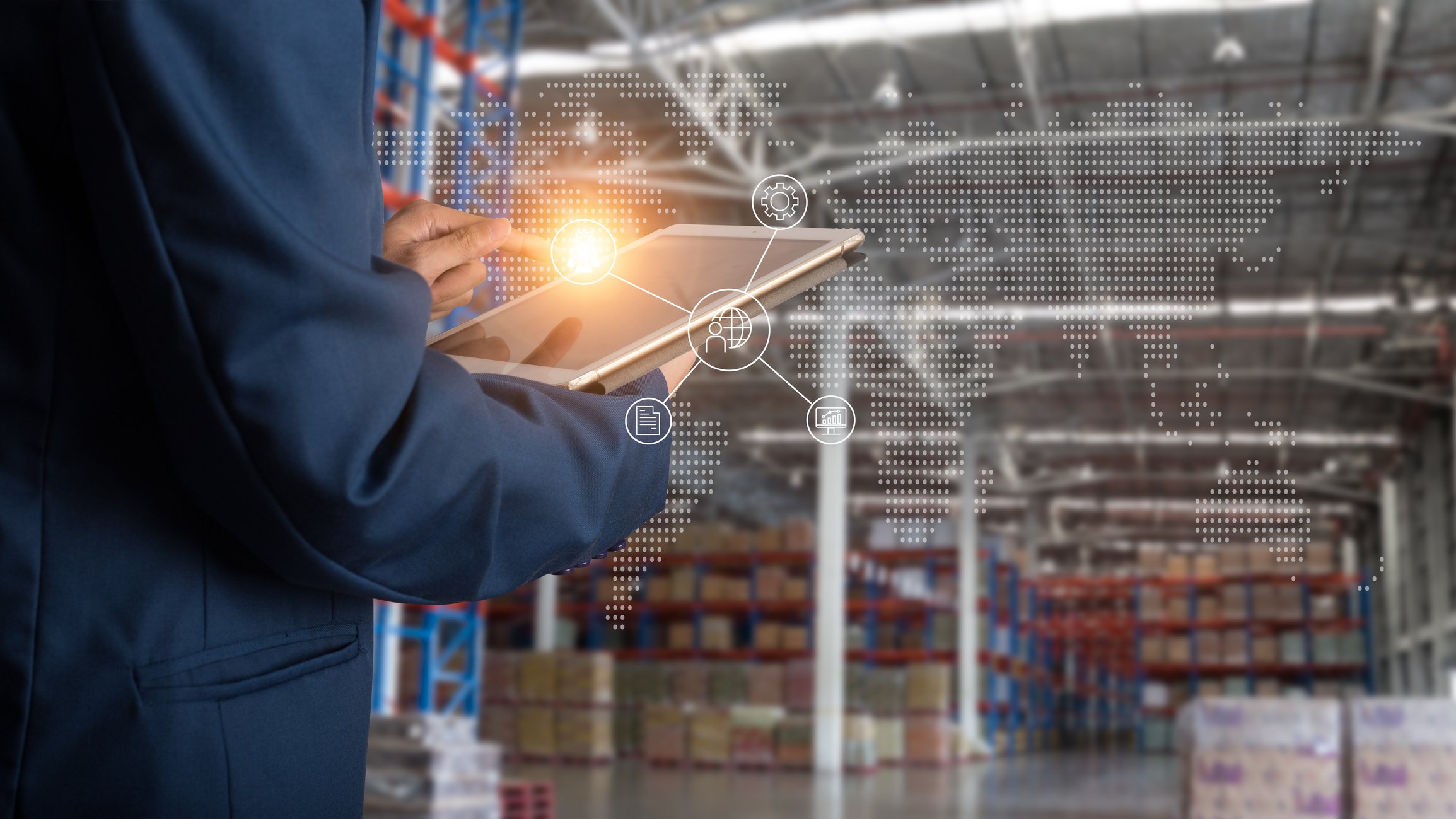 Shot from behind a man holding a tablet in a modern warehouse and a light illuminates from the tablet. 