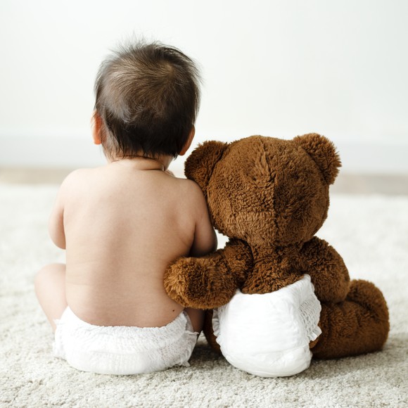 A baby sitting beside a teddy bear; both are wearing a diaper