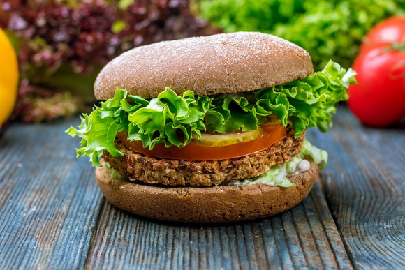 A veggie burger with lettuce and tomato sits on a wooden surface.