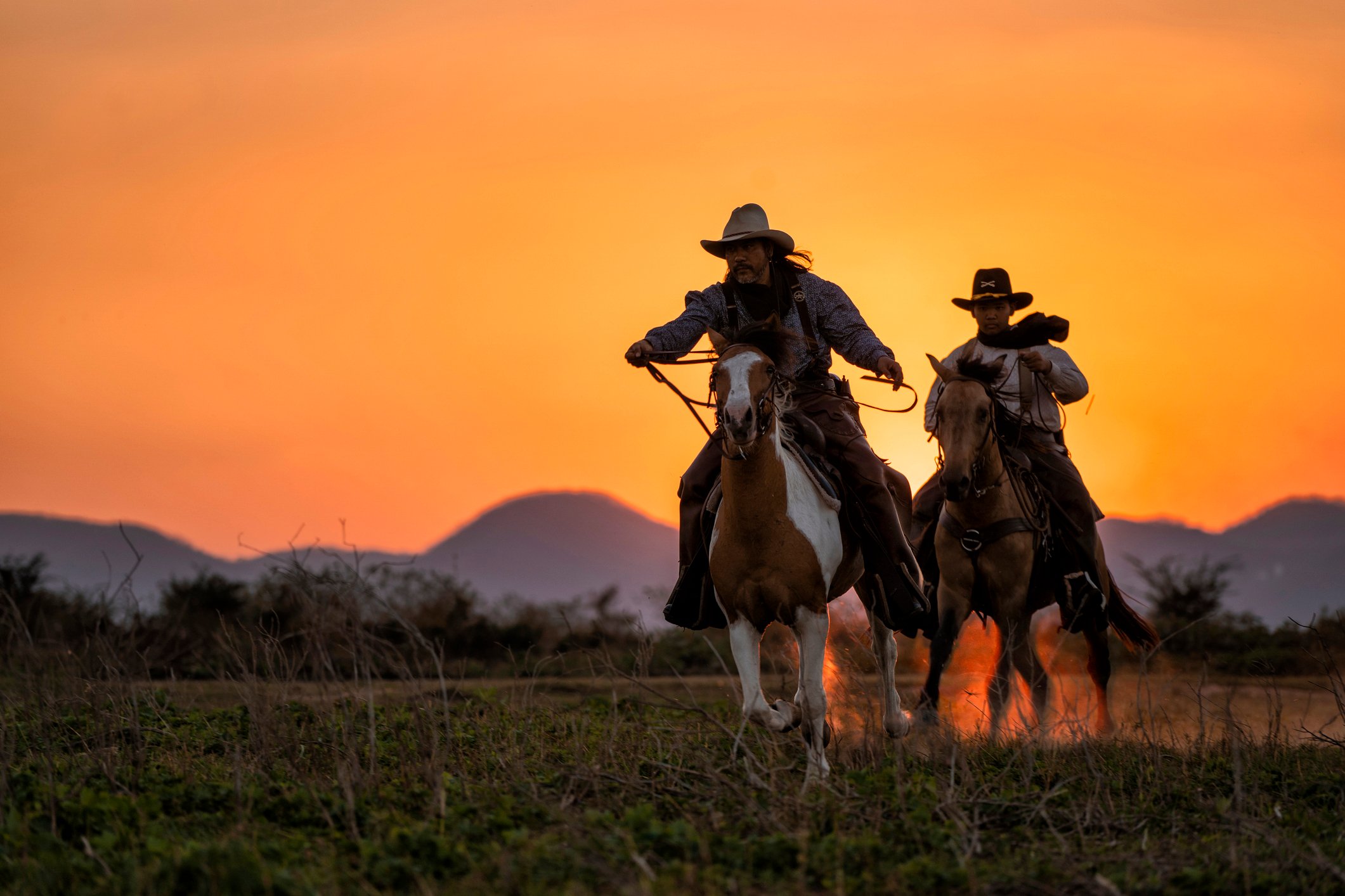 Two cowboys on galloping horses at sunset