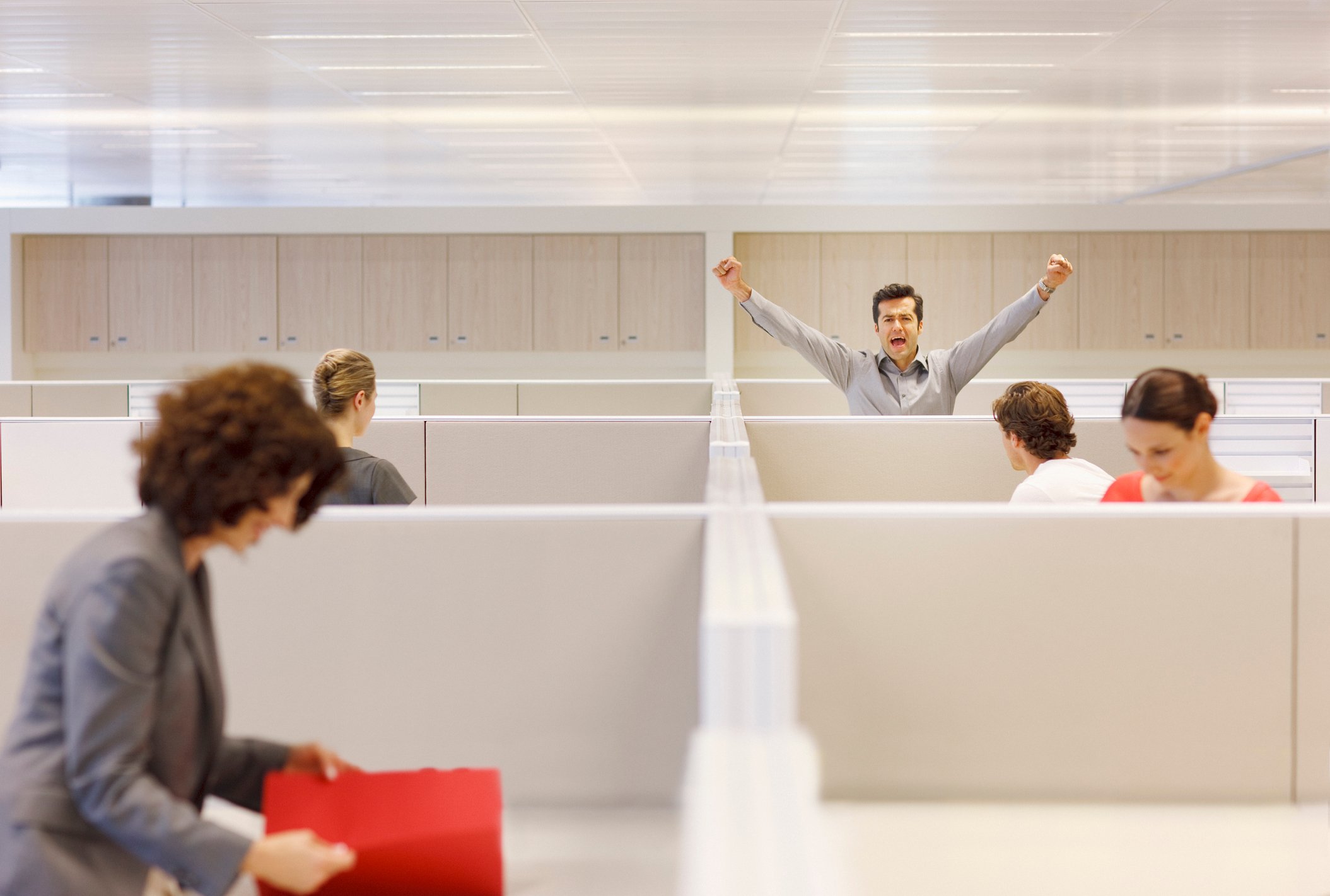 A man in an office cubicle cheering as his colleagues go about their work