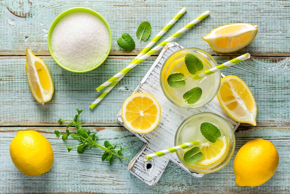 A rustic presentation of lemonade glasses on a wooden table, surrounded by fresh lemons and herbs.