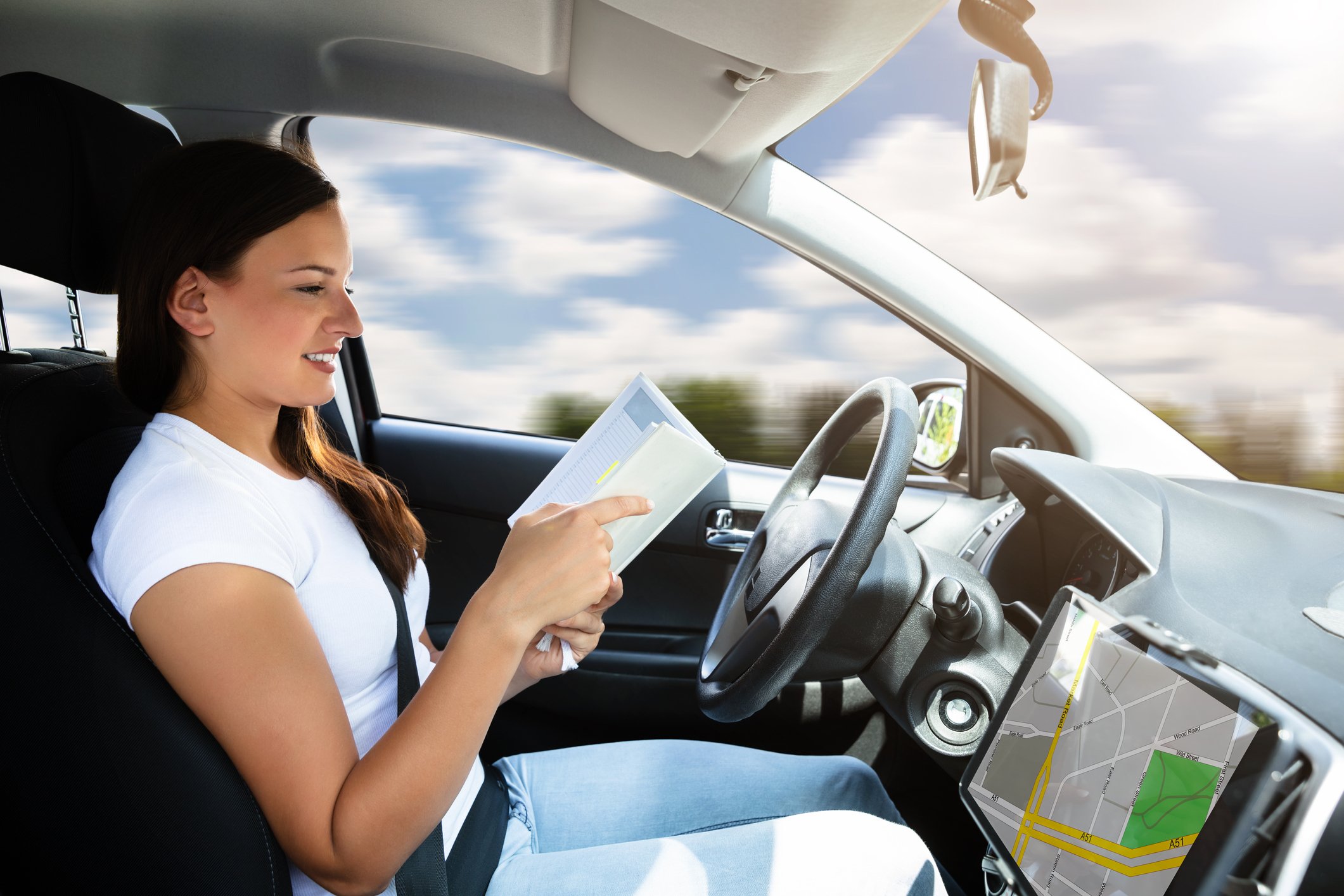 A woman sitting in the driver's seat of a car, reading a book