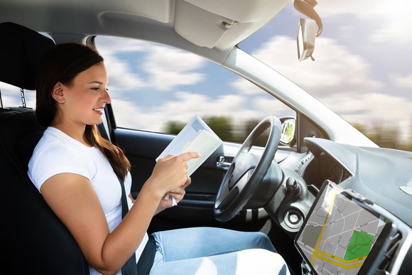 A woman sitting in the driver's seat of a car, reading a book