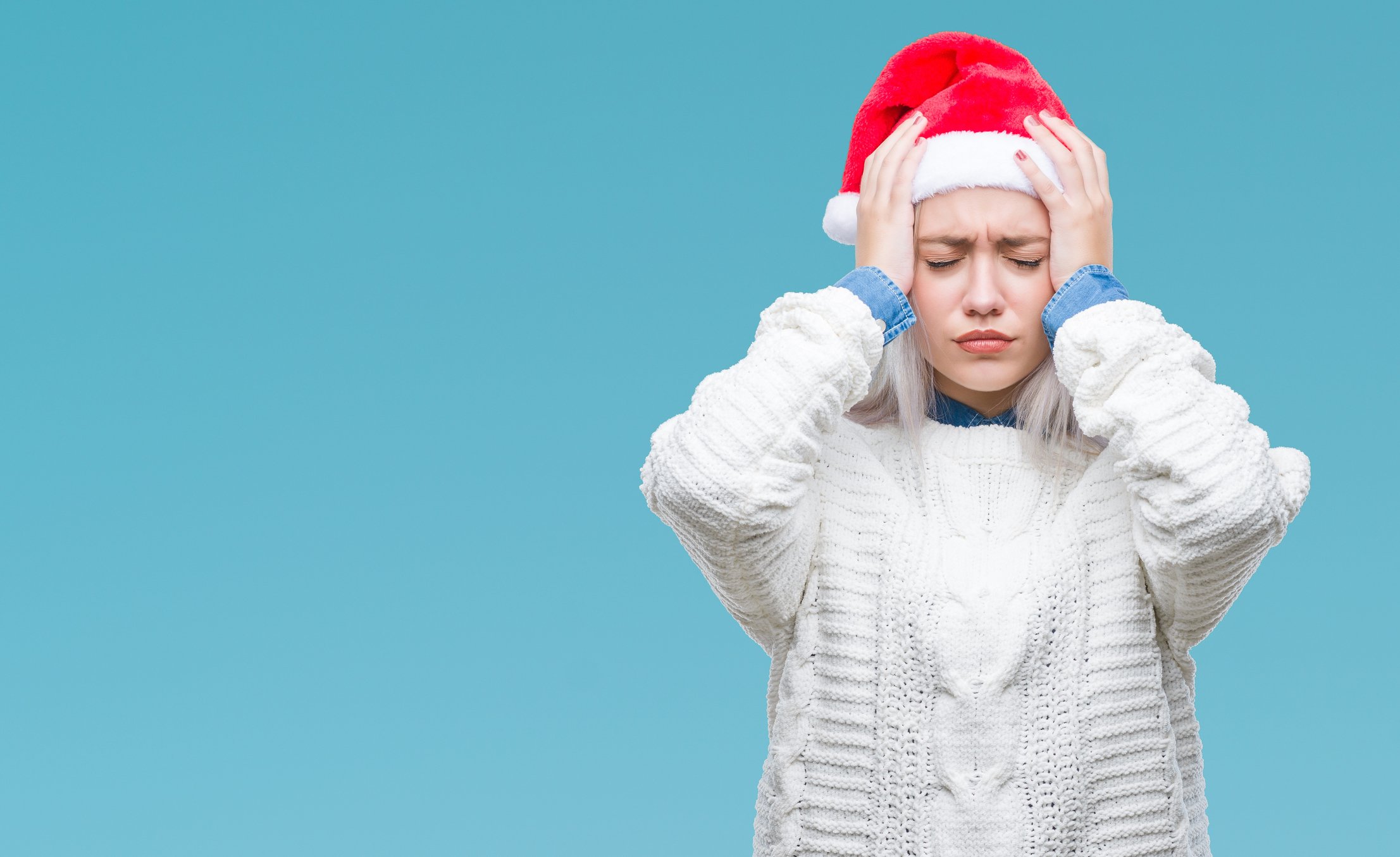 A frustrated woman in a Santa cap places her hands on her head.