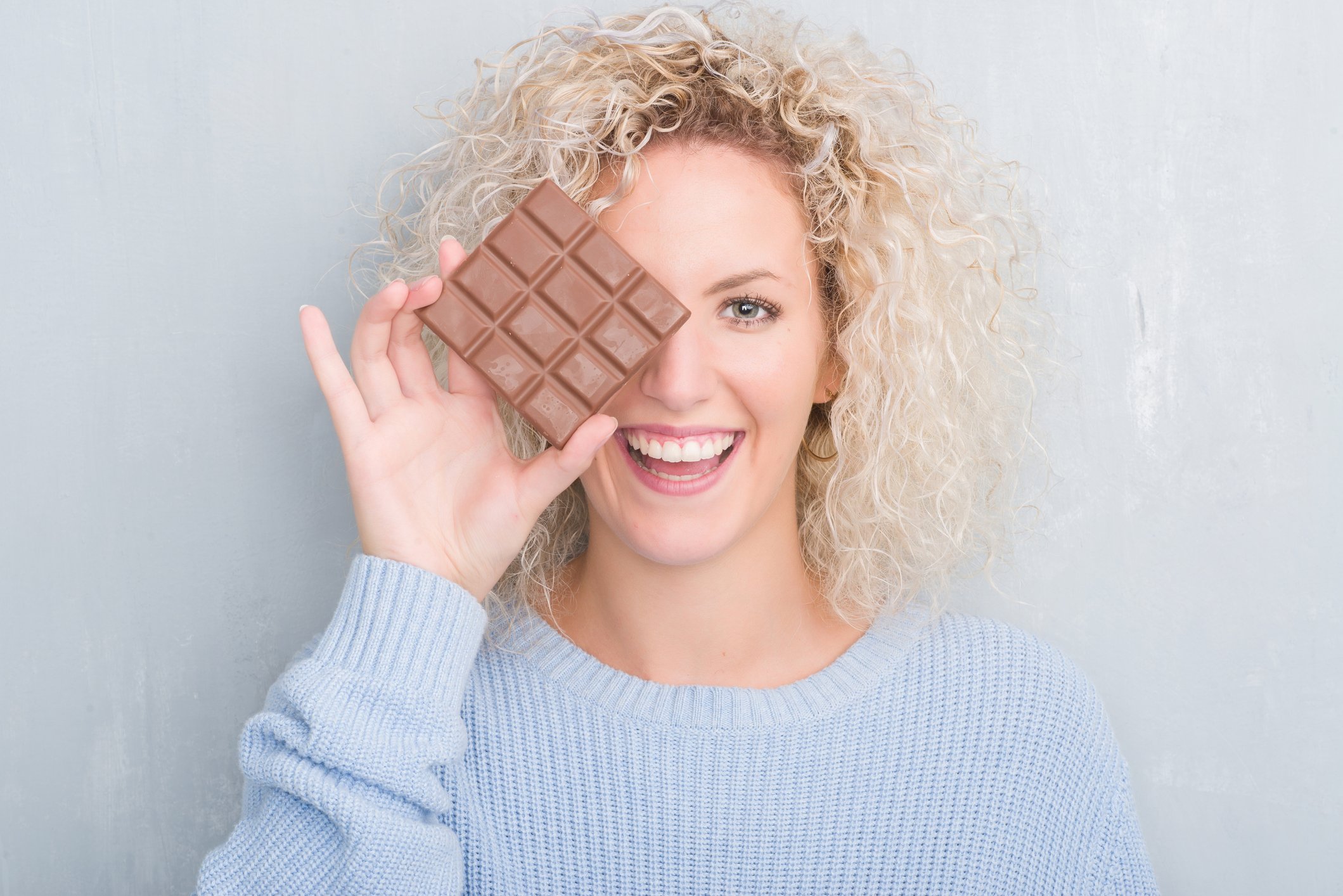 A woman smiles while holding a chocolate bar.