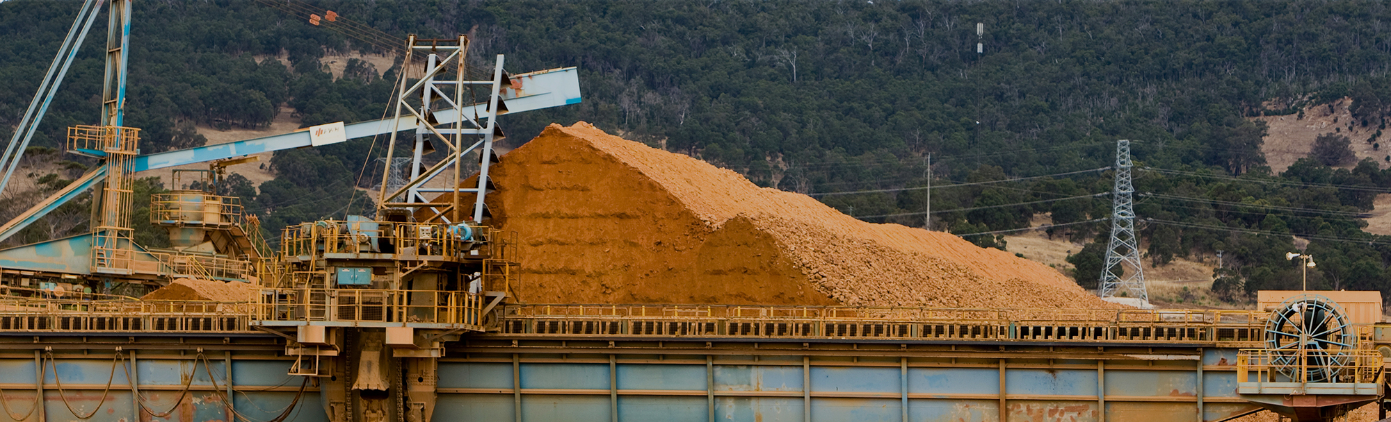 Pile of bauxite raw at a production facility, with cranes and conveyers nearby.