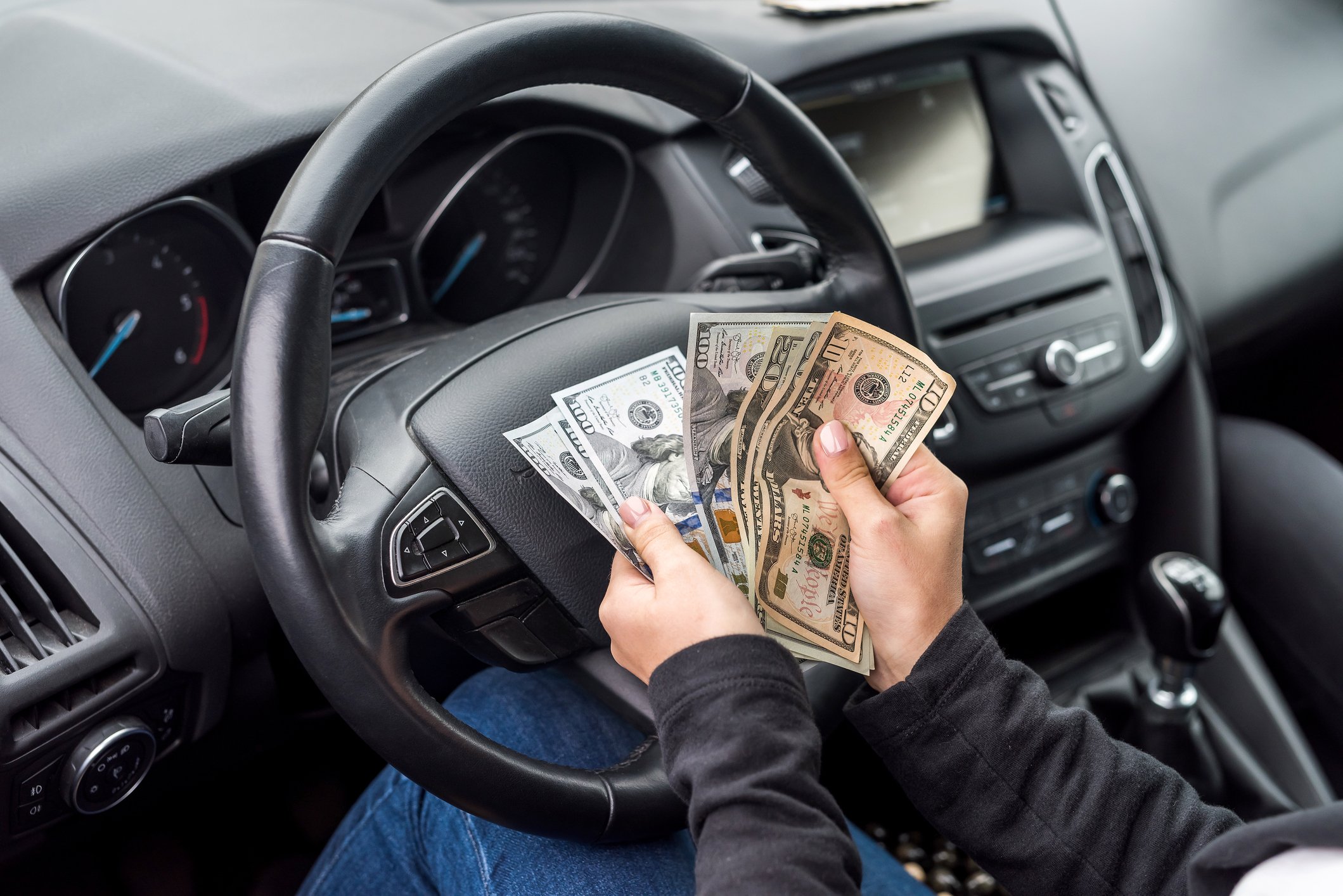 A woman's hands holding paper currency in front of a car's steering wheel