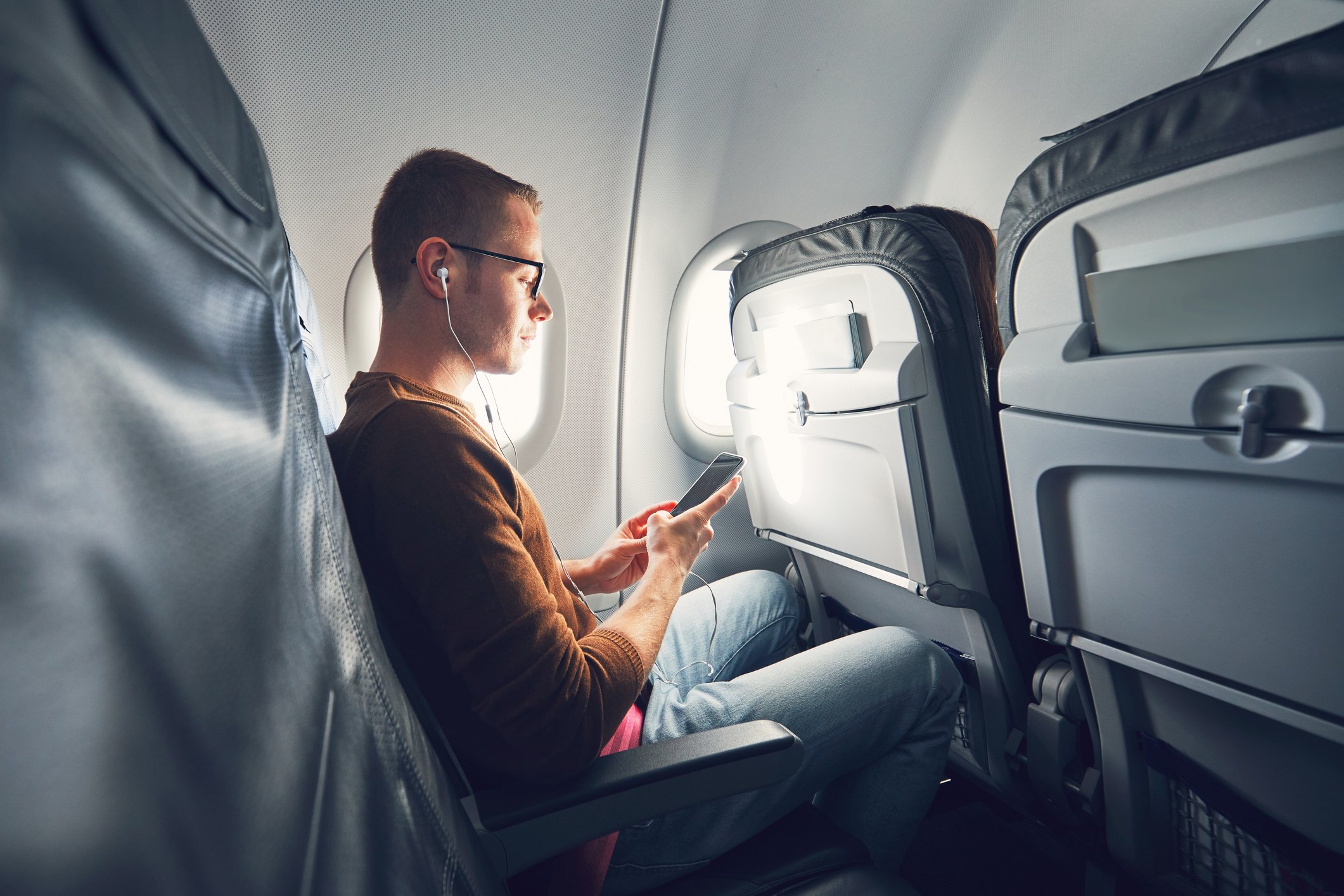 A young man using his smartphone while seated in an airliner.