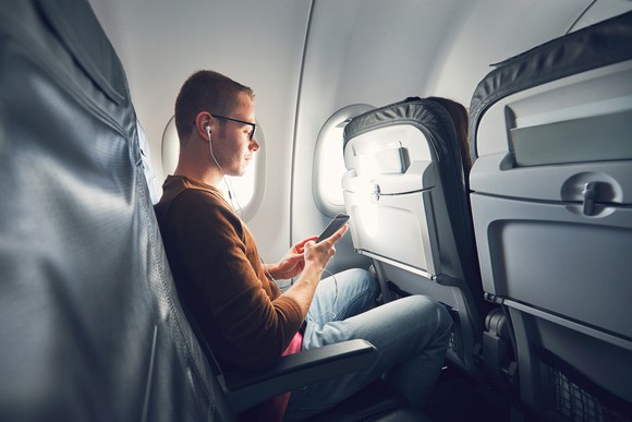 A young man using his smartphone while seated in an airliner.
