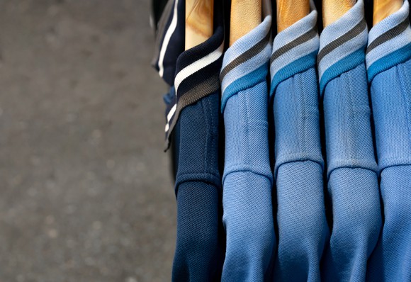Polo-style shirts in navy and light blue hang on hangers in a shop.