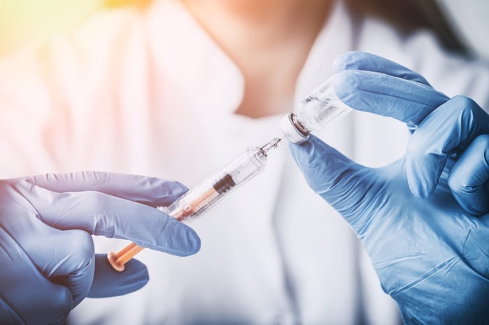 Female wearing a white coat holding a syringe and vaccine vial 