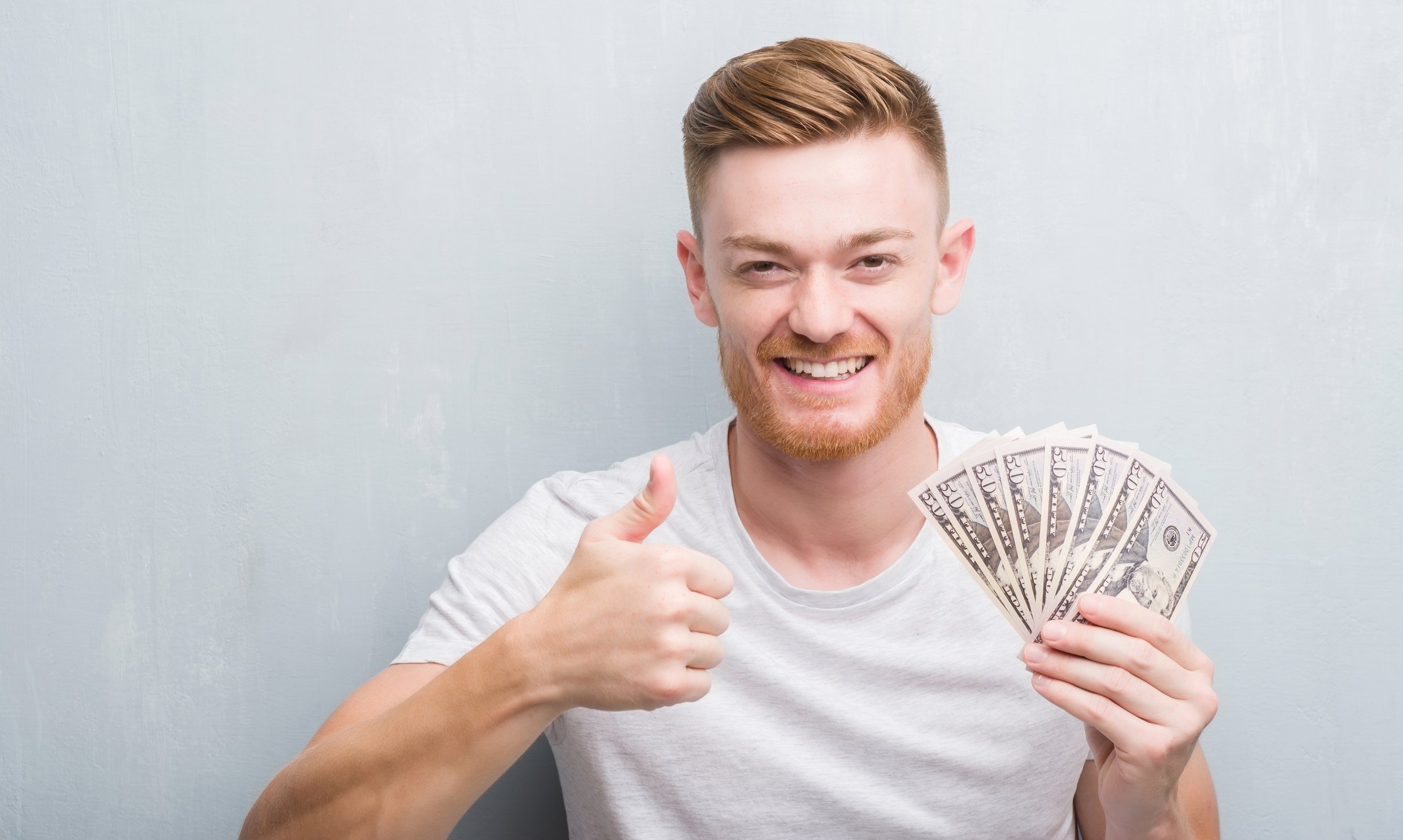 Man holding money in one hand, giving thumbs up with the other.