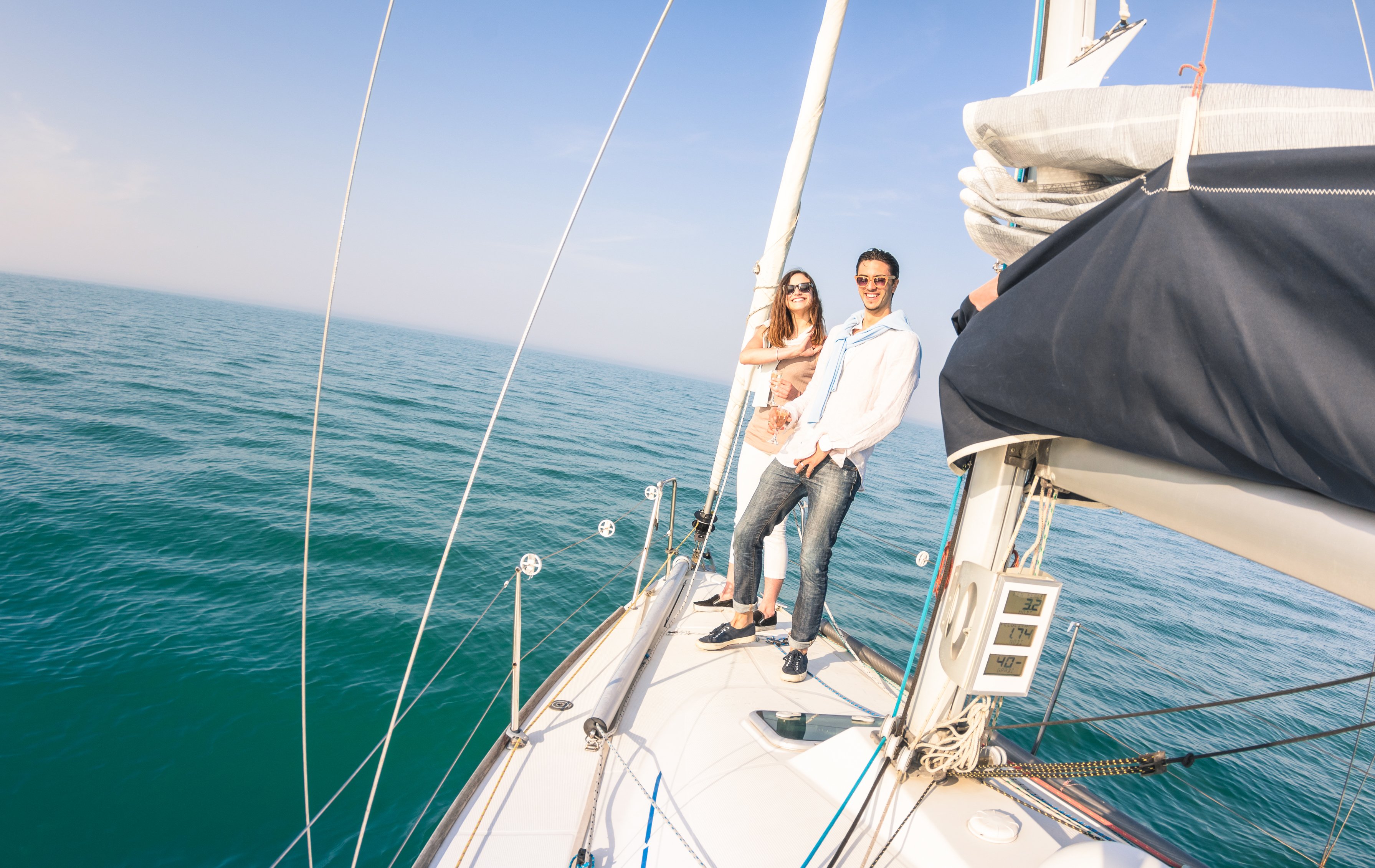 A young couple stands on the bow of a sailboat on the ocean. 