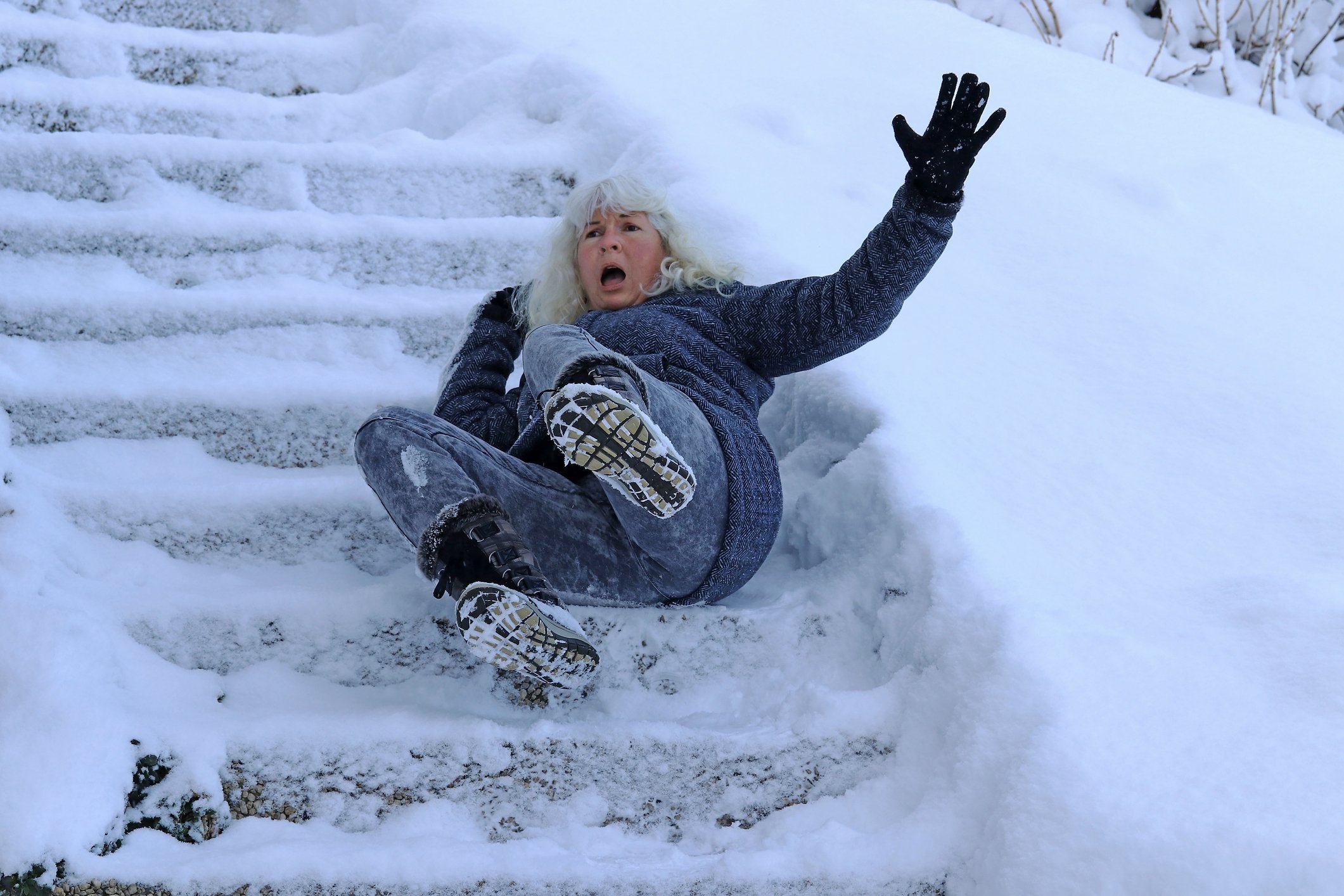 An older woman falling down a flight of snowy steps outdoors