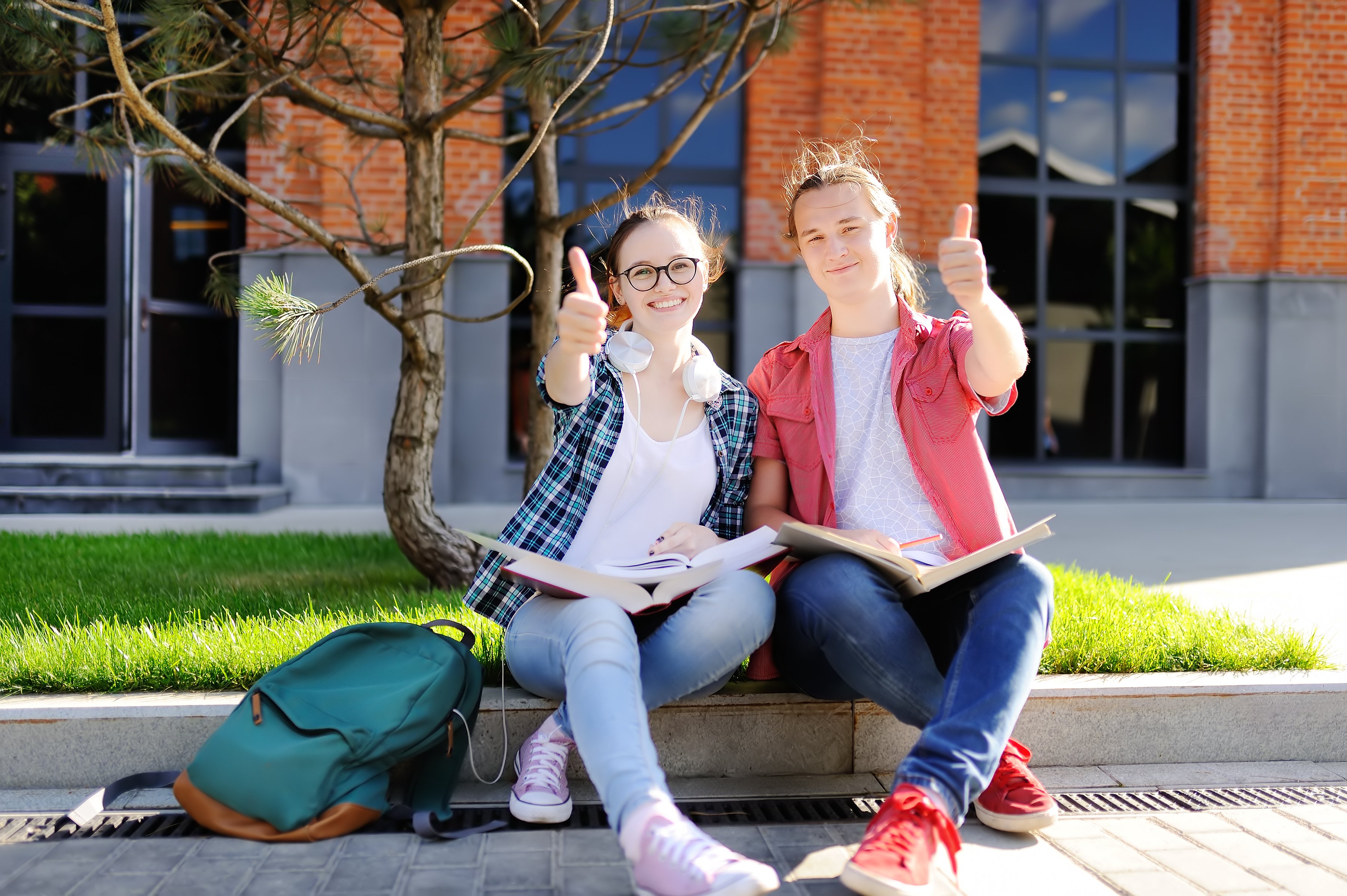 Two students with textbooks in laps, giving thumbs-up.