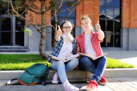 Two students with textbooks in laps, giving thumbs-up.