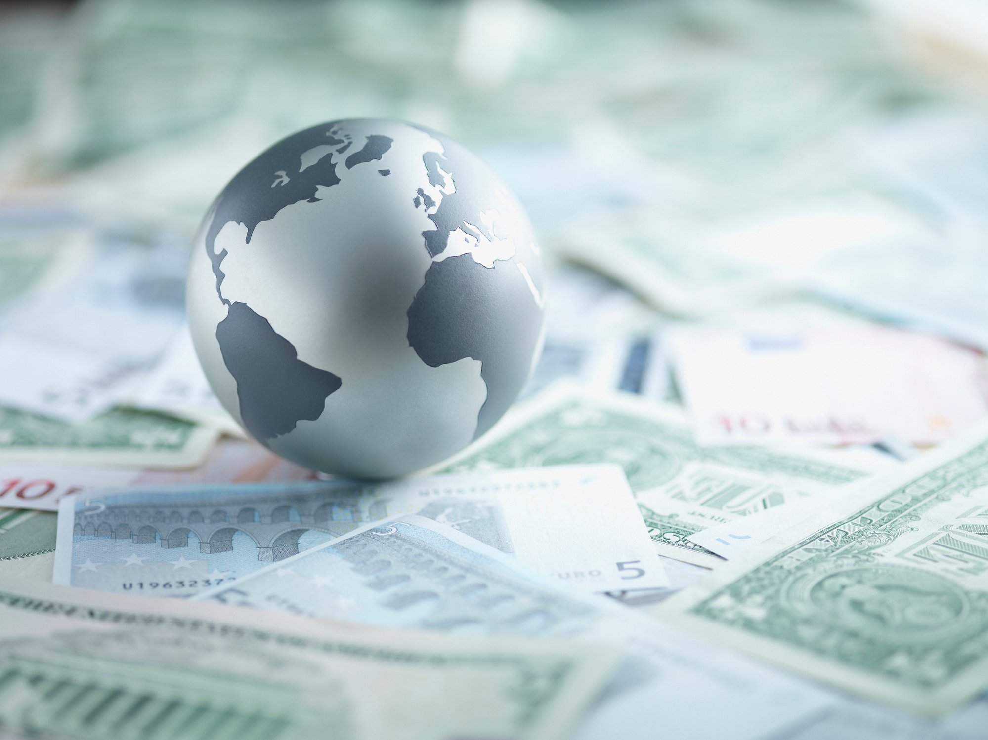 A miniature globe on top of different currencies.