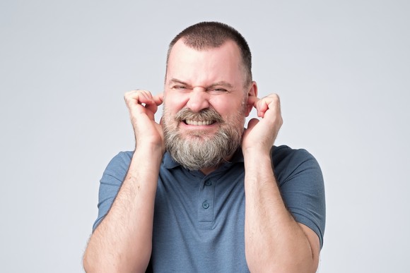 Man grimacing with his fingers in his ears