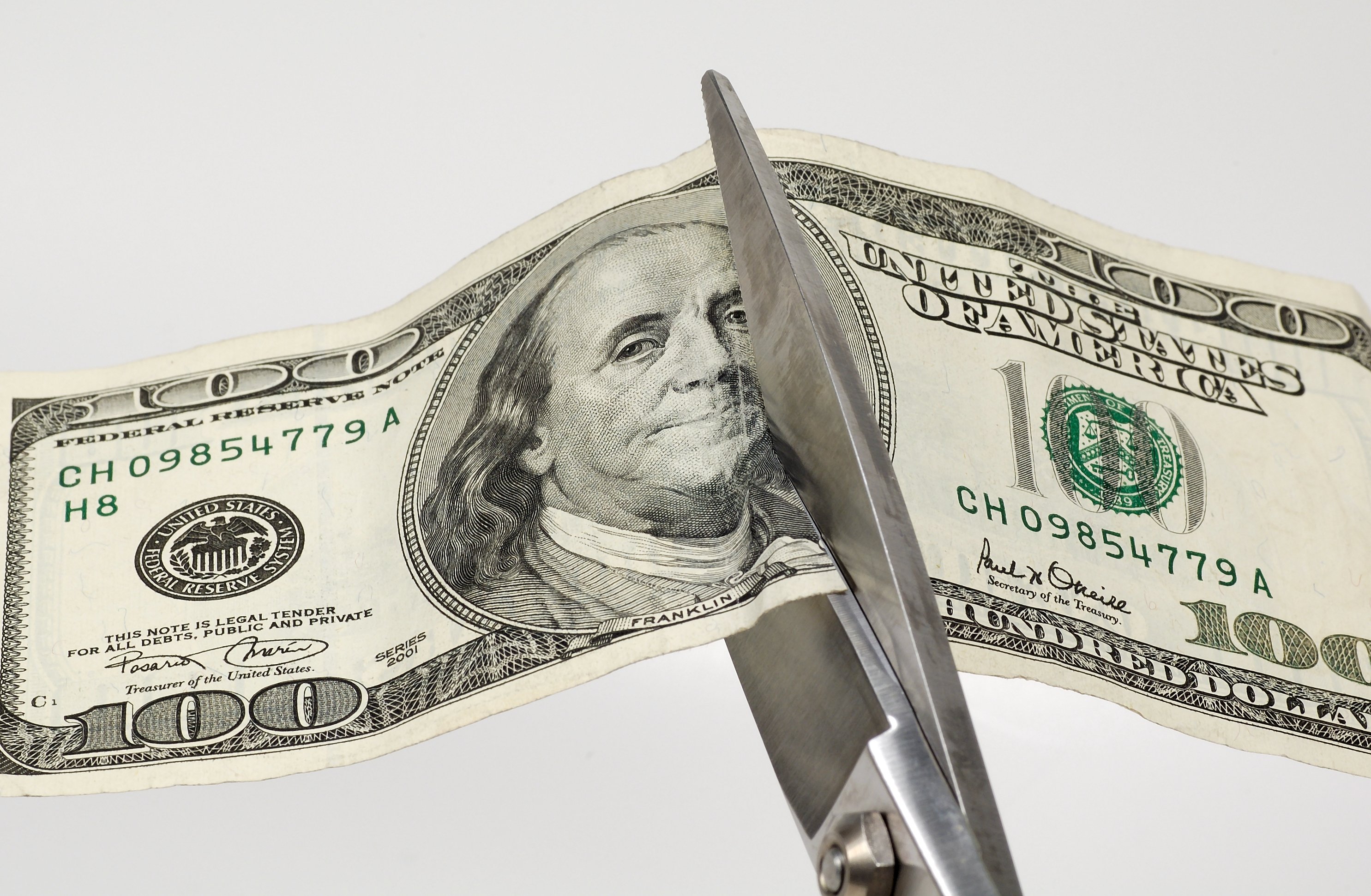 Scissors cutting a one hundred dollar bill in half.